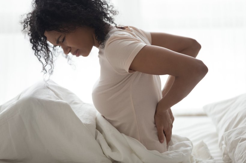 Eine Frau sitzt auf dem Bett und hält sich vor Rückenschmerzen den Rücken