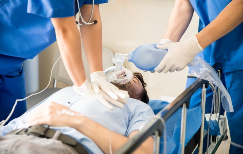 Zwei Mediziner in blauen Kasacks versuchen, einen Patienten auf einer Trage...
