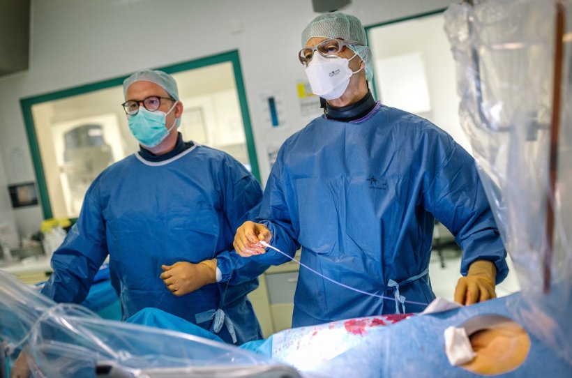 Zwei Kardiologen in blauer OP-Kleidung führen einen Katheter in das Herz eines...