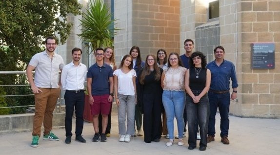 A group photo of twelve people standing in the courtyard of an academic building