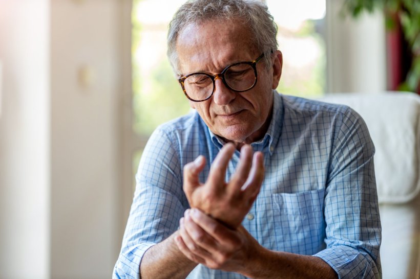 Ein älterer Mann mit Brille betastet sein rechtes Handgelenk mit der linken...