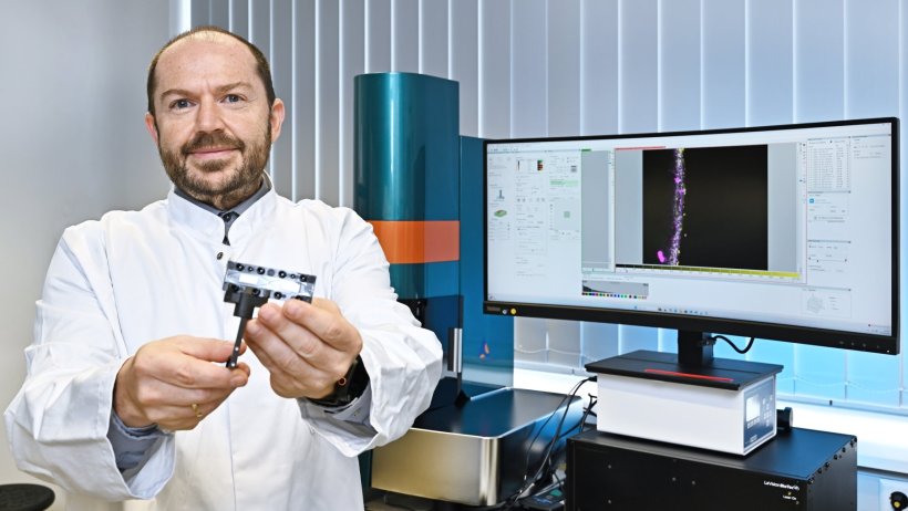 Prof. Dr. Alexander Mosig steht neben einem Tisch, auf dem ein breiter...