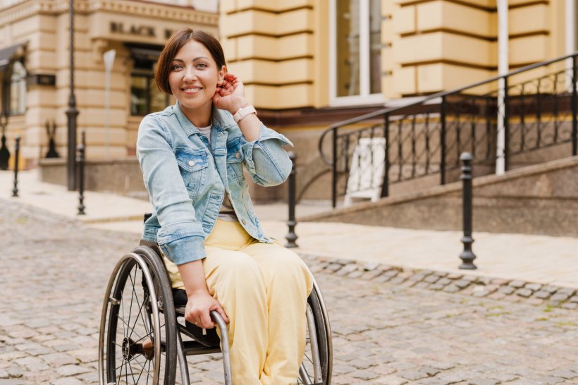 Eine junge Frau sitzt in der Stadt in ihrem Rollstuhl und lächelt in die Kamera