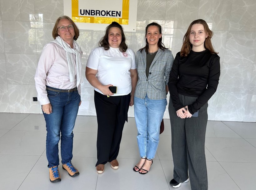 Vier Frauen stehen für ein Gruppenfoto nebeneinander in einer Reihe. Im...