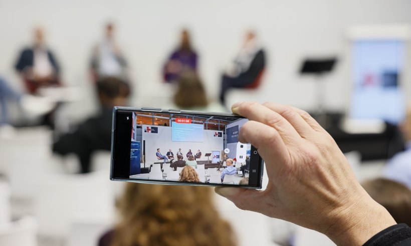 Eine Hand hält ein Smartphone, um ein Video eines Panels aufzunehmen. Die...