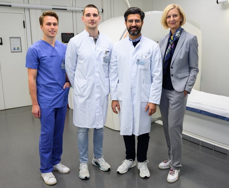 Vier Personen stehen für ein Teamfoto vor einem medizinischen bildgebenden...