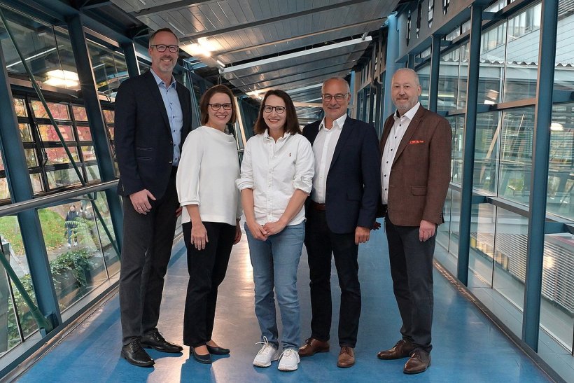 Fünf Personen stehen für ein Gruppenfoto in einem Verbindungsgang mit...