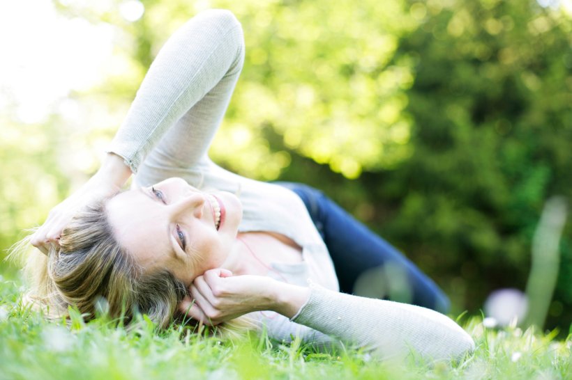 Eine Frau liegt auf der Wiese und schaut lächelnd in den Himmel