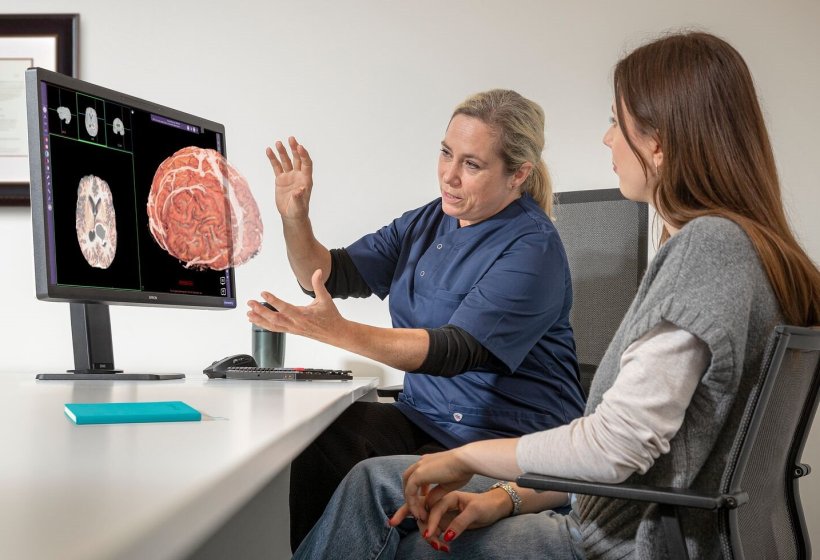 A doctor and her patient are sitting at a table in front of a computer screen....