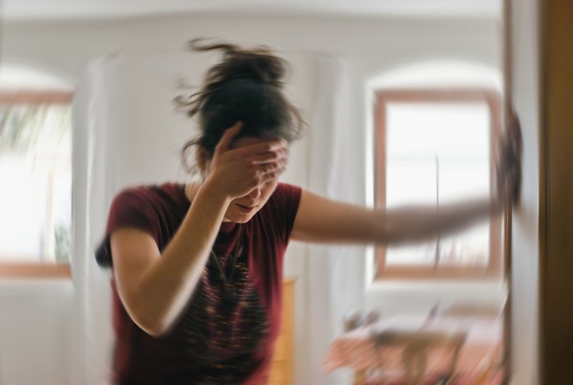 Eine Frau mit Schwindel hält sich mit der rechtan Hand die Stirn und stützt...