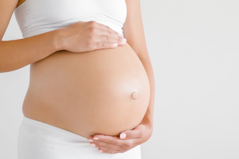 Eine schwangere Frau hält ihren Bauch schützend mit beiden Händen
