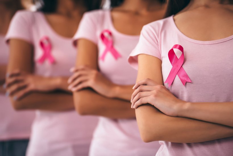 Four women in pink shirts with arms crossed wearing pink ribbons for breast...