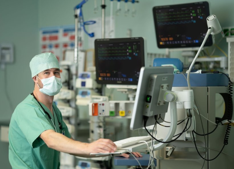 Dr. Jakob Wittenstein steht im grünen Kasack mit OP-Haube und Schutzmaske in...