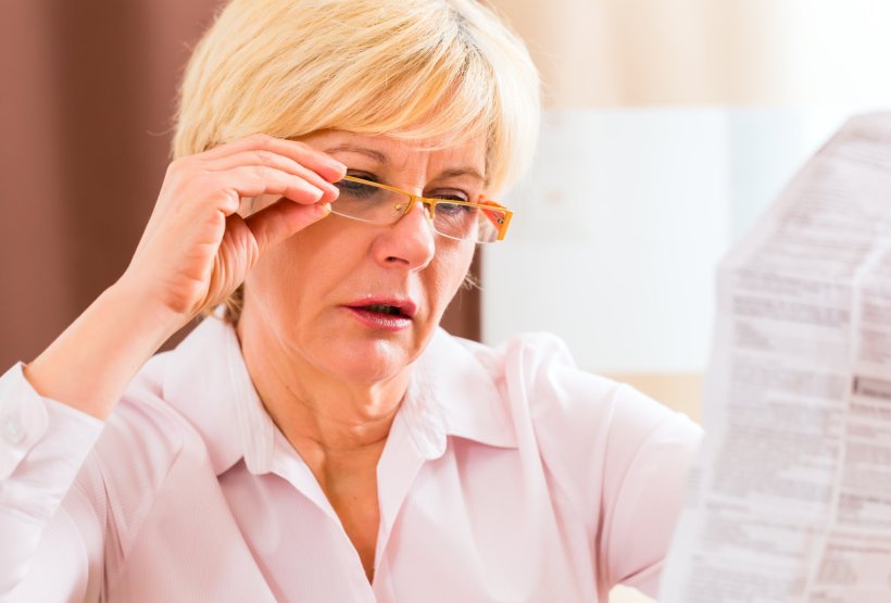 Eine Senioron liest einen Beipackzettel für ein Medikament. Sie hält mit der...
