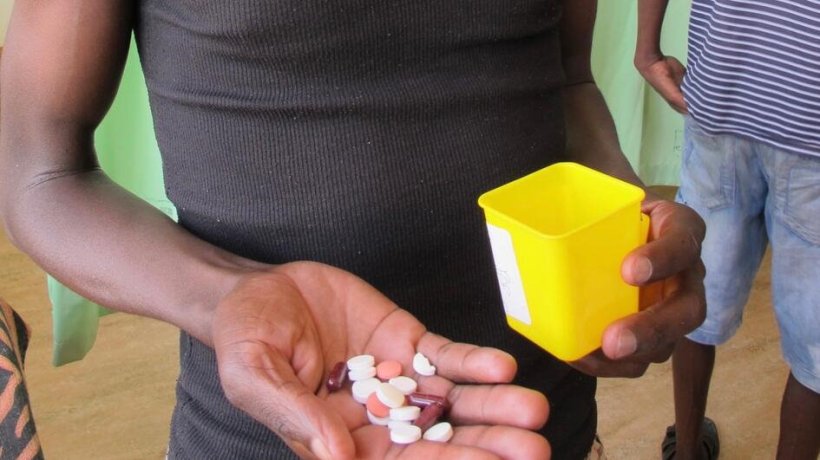 EIn Mann hält mehrere Tabletten in seiner rechten Hand, in der Linken einen...