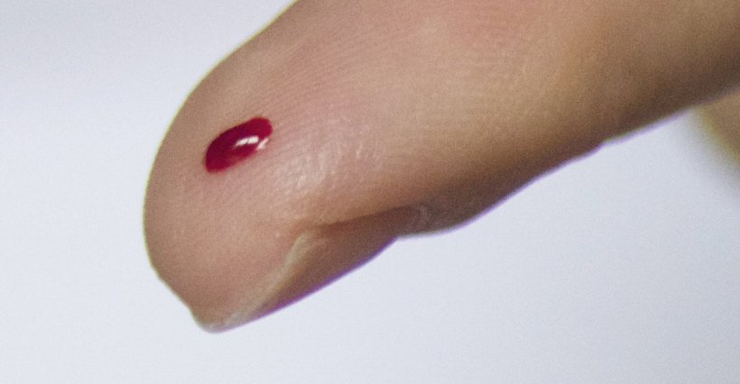 Closeup photo of a finger with a small drop of blood on its tip