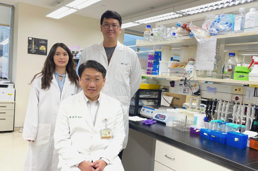 Three scientists in white lab coats are sitting and standing in a laboratory...