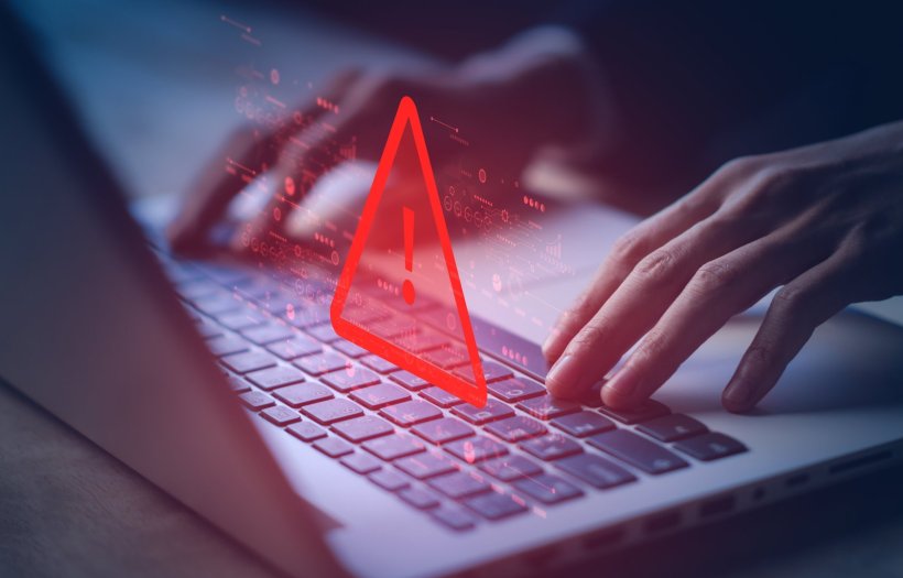 Hände auf einer Laptop-Tastatur, auf der ein rotes dreieckiges Warnsymbol...