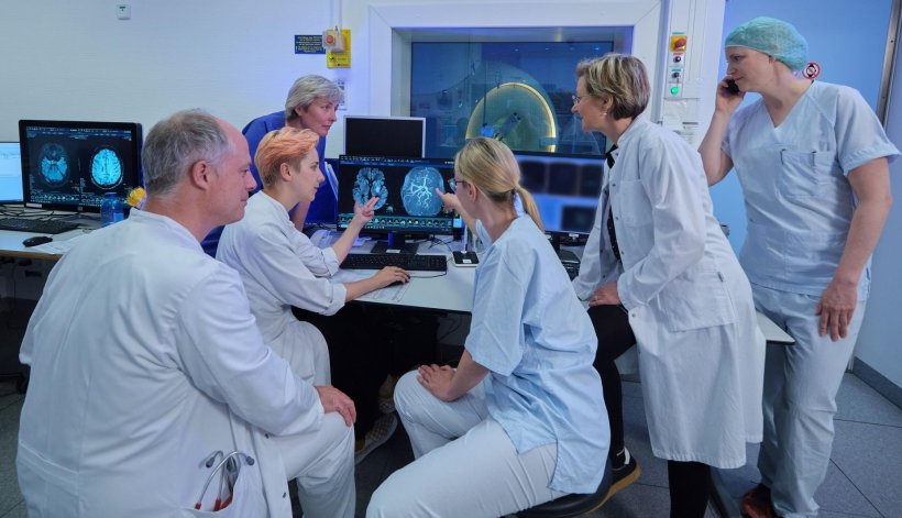 Sechs Personen sitzen und stehen in der Neuroradiologie um einen Tisch mit...