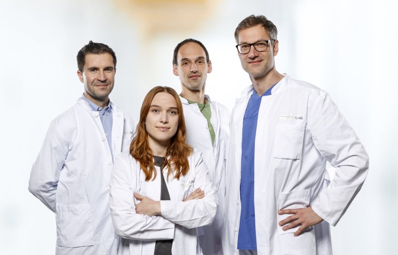 Vier Mediziner in weißen Arztkitteln stehen für ein Teamfoto vor einem hellen...