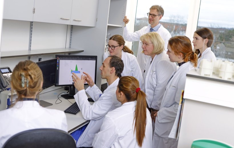 Acht Mediziner bei einer Besprechung in einem Laborraum. Alle blicken auf einen...