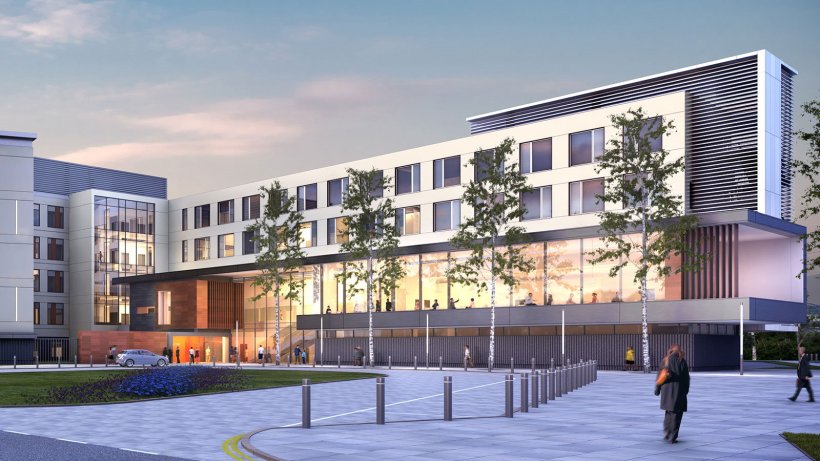 A modern hospital building, with four slender trees in front of the main...