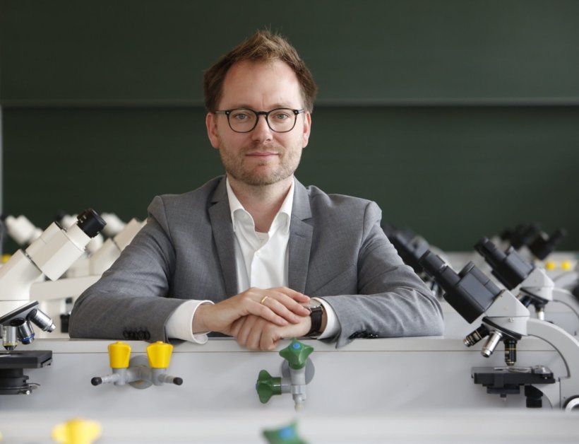 Professor Kilian Schober sitzt an einem Tisch mit Laborarmaturen und Mikroskopen