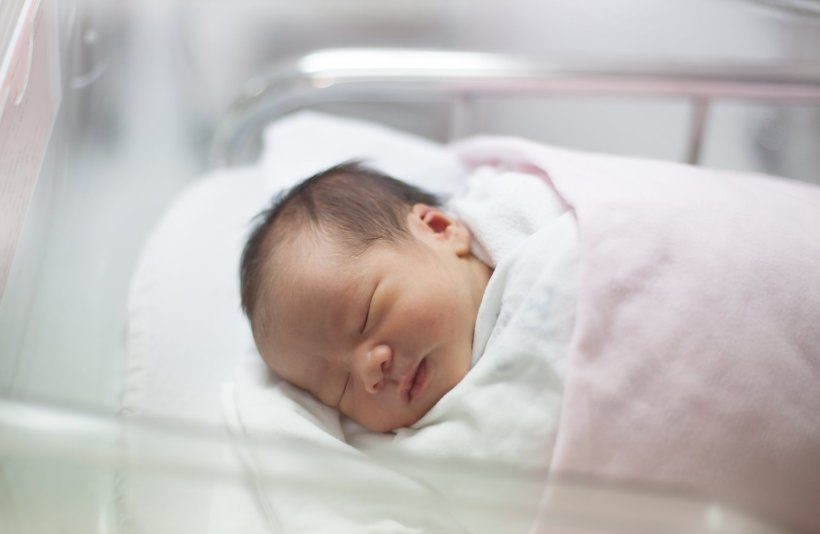 A newborn infant asleep in a blanket in the delivery room of a hospital