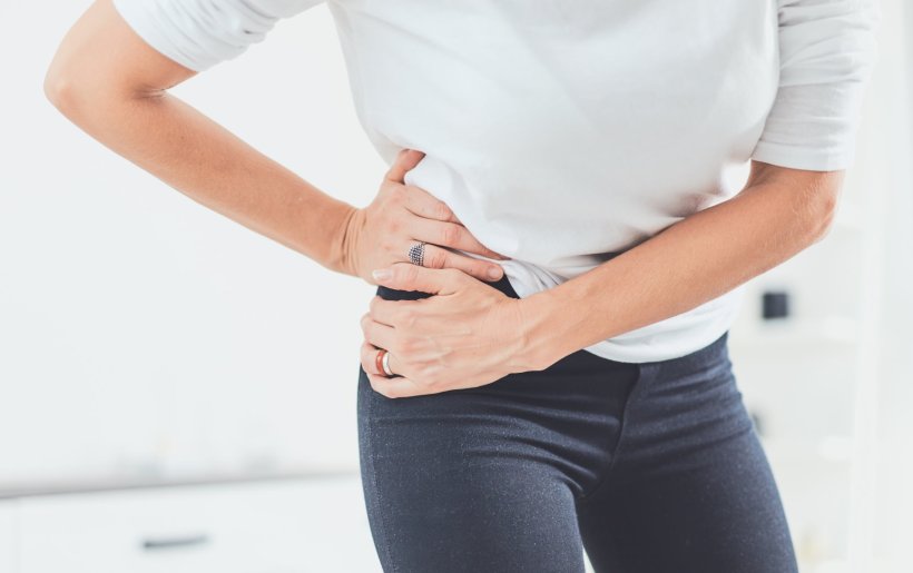 A woman in a white shirt and dark pants is holding her right hip with both...