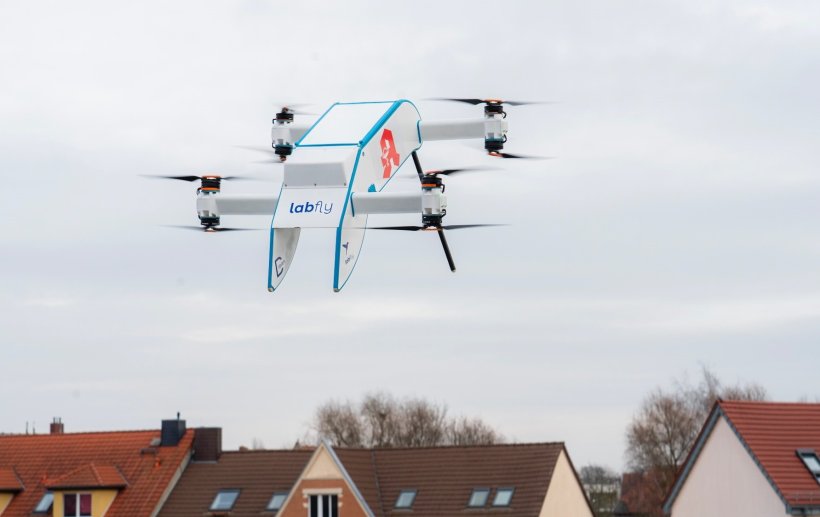 Eine Drohne mit vier Rotoren und Apotheken-Logo auf dem Rumpf fliegt über...