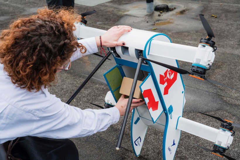Eine Frau legt ein Paket in die geöffnete Bodenklappe einer Drohne mit...