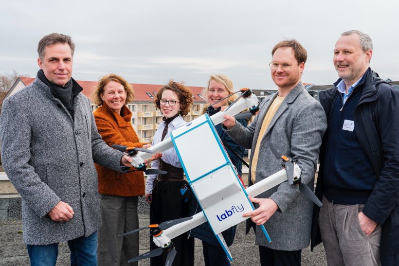 Sechs Personen stehen für ein Gruppenfoto nebeneinander. In der Mitte halten...