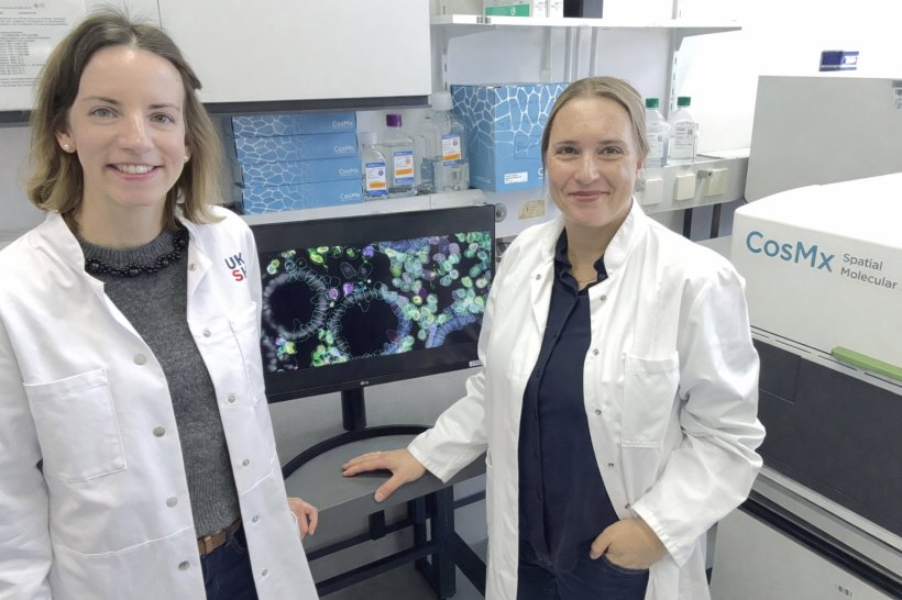 Zwei Frauen in weißen Laborkitteln stehen neben einem Computermonitor in einem...