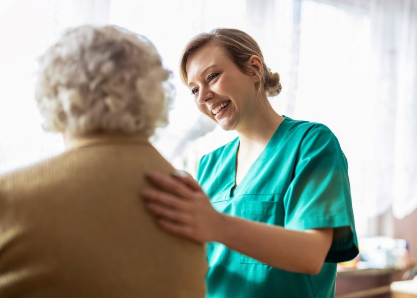 Eine lächelnde Medizinerin im grünen Kasack spricht ermutigend mit einer...