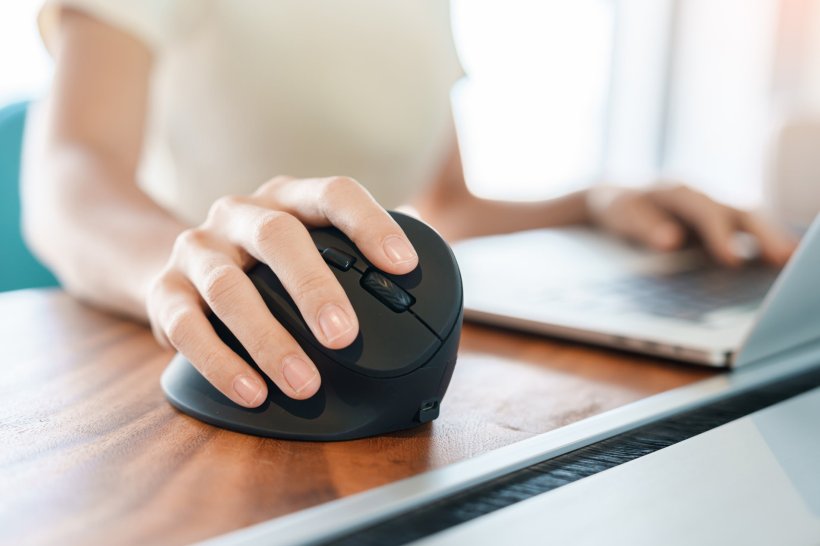 Closeup photo of a woman using a black ergonomic mouse while working on her...