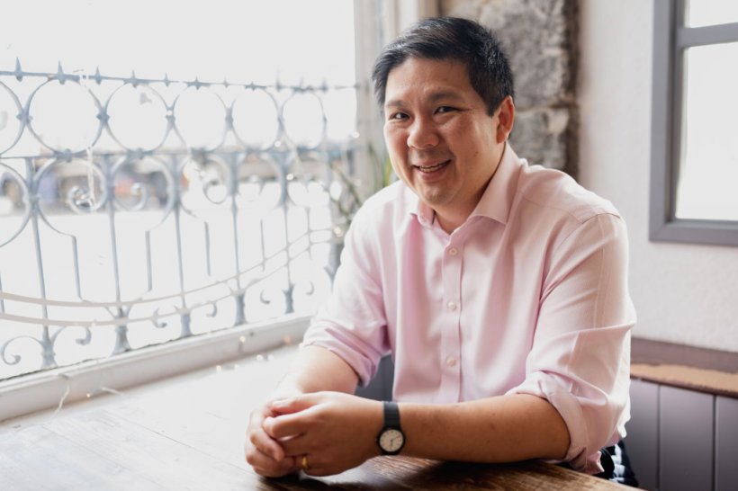 Professor Gerald Lip is sitting at his desk in front of a window with an ornate...