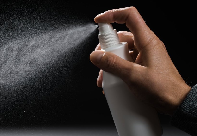 Closeup photo of a hand using a spray bottle. The bright spray particles are...