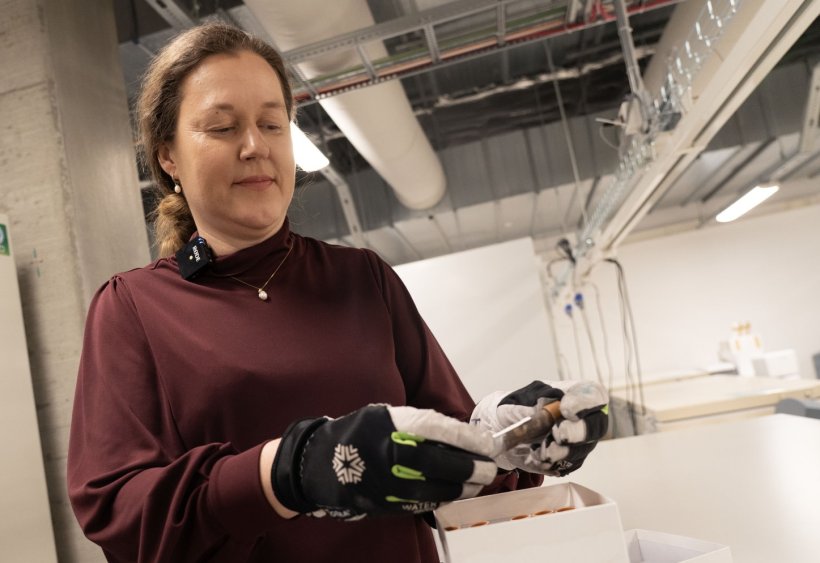 A woman is standing in a laboratory in front of a white box, handling a...