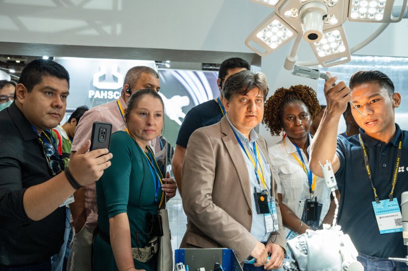 A group of people at a medical tradefair, looking at an operating table and...