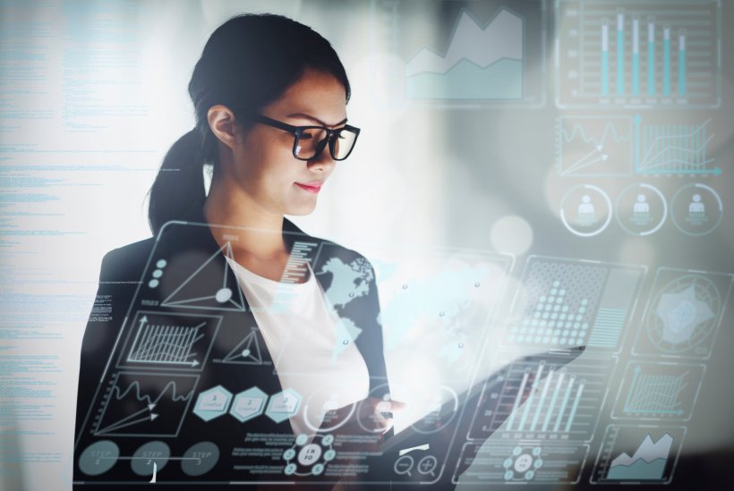 Eine junge Frau im Business-Look blickt auf ihr Tablet herab. Über das ganze...