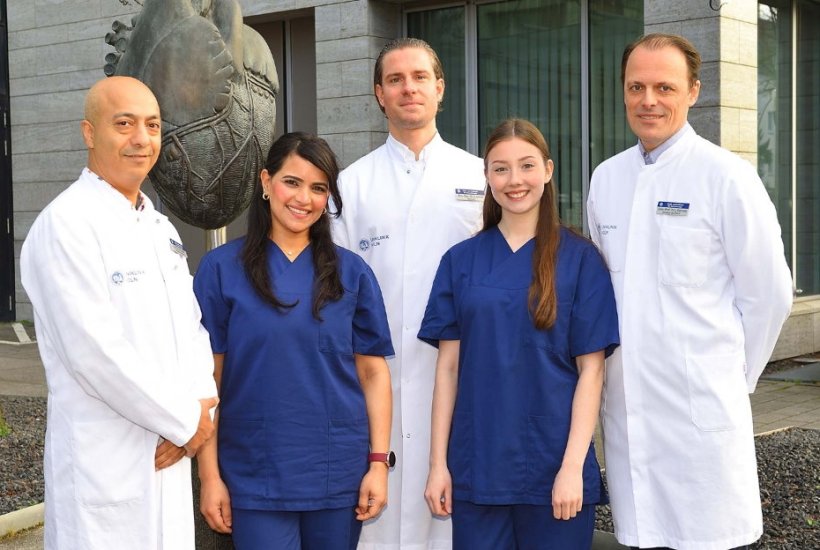 Fünf Personen stehen in einer Reihe für ein Teamfoto. Im Hintergrund ist eine...