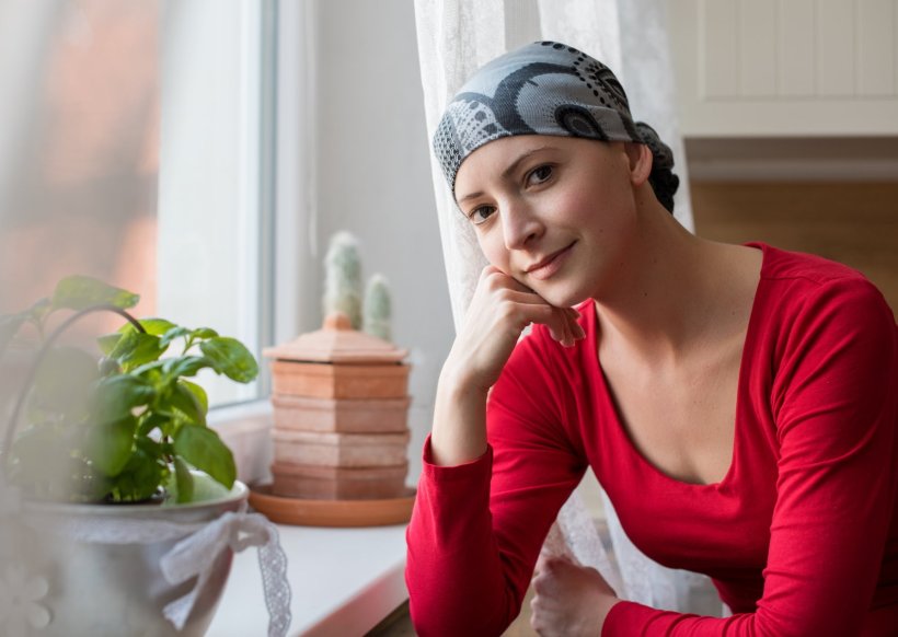 A young woman wearing a bandana, sittings at a window. She is looking...