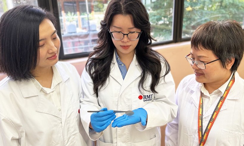 Three researchers in white lab coats standing next to each other. The woman in...