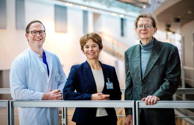 Drei Personen stehen für ein Teamfoto an einem schmalen Metallgeländer im...