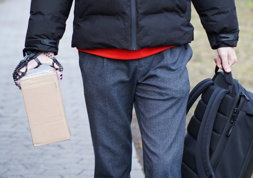 Eine Person mit bionischer Orthese an der rechten Hand hält ein kleines Paket....