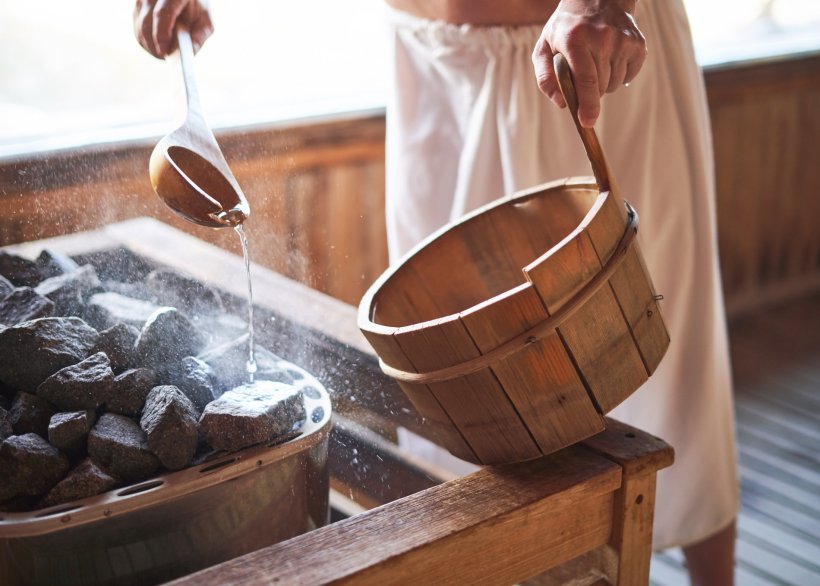 A man in a sauna is pouring water on hot rocks to produce steam