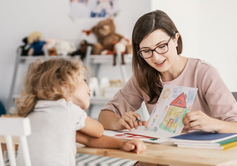 Eine Frau und ein junges Mädchen sitzen sich an einem Tisch gegenüber. Die...