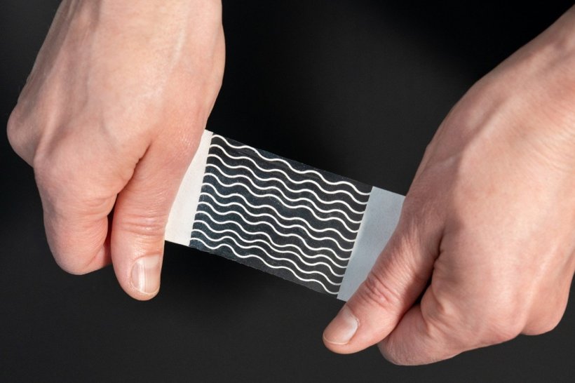 Zwei Hände halten eine dünne Folie, auf der weiße Wellenlinien aufgedruckt...