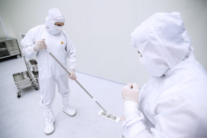 Two men in white full-body suits are thoroughly cleaning the cleanroom of a...