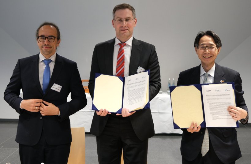 Drei Männer stehen mit aufgeklappten offiziellen Dokumenten nebeneinander, um...